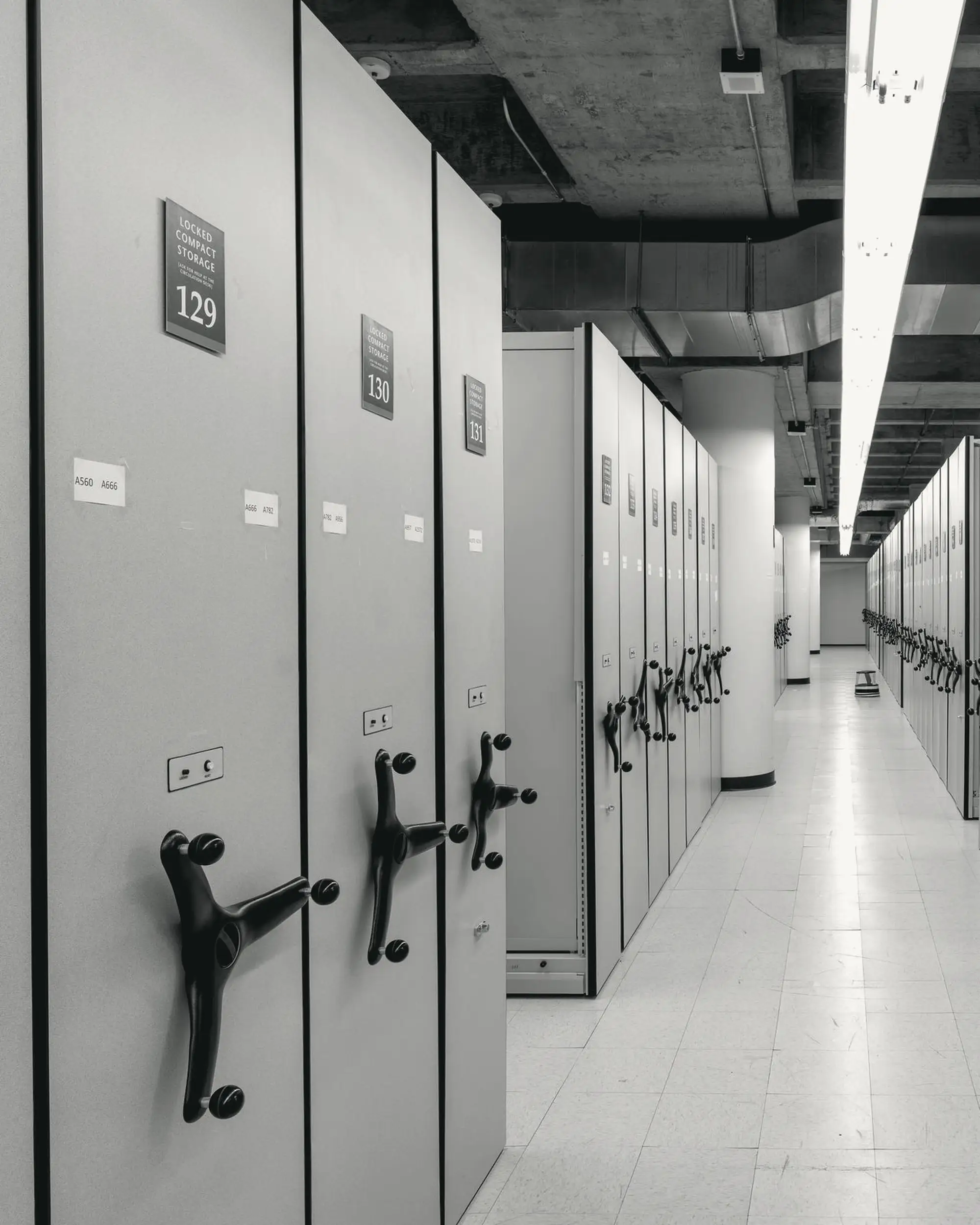 Aisle of rolling compact shelving in central perspective, cold ceiling light.